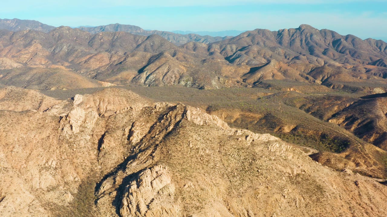 Cabo Pulmo mountain landscape with a rugged lower ridge, shadowed cuts in the terrain, rolling brown hills, far ridgelines, blue sky, and no visible people.
