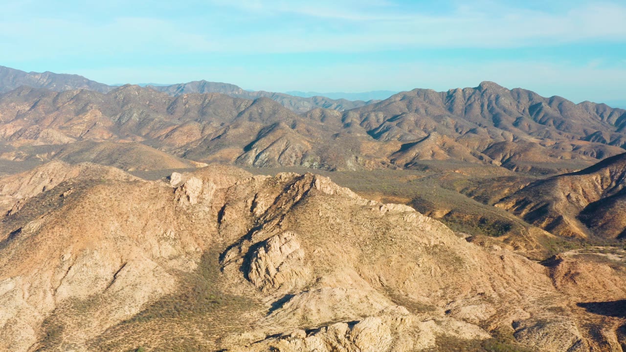 Fourth frame keeps the wide Cabo Pulmo aerial composition, with a large rocky foreground ridge, shadowed folds to the right, and no visible people.