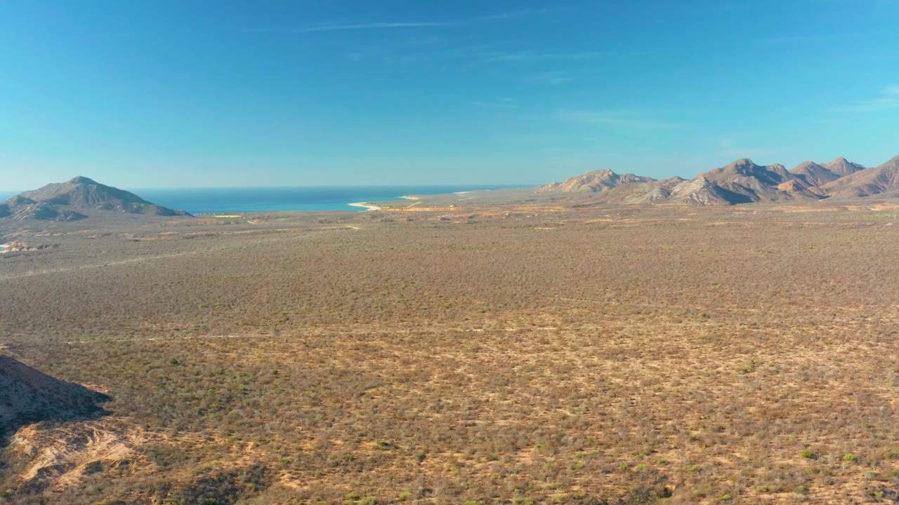 Cabo Pulmo frame with a broad arid plain across the foreground, distant coastline near the center, mountains at the right horizon, and no visible people.