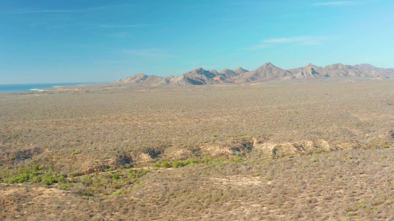 The Cabo Pulmo terrain appears from above with tan scrub, green patches in shallow washes, distant mountains, a level horizon, and no visible people.