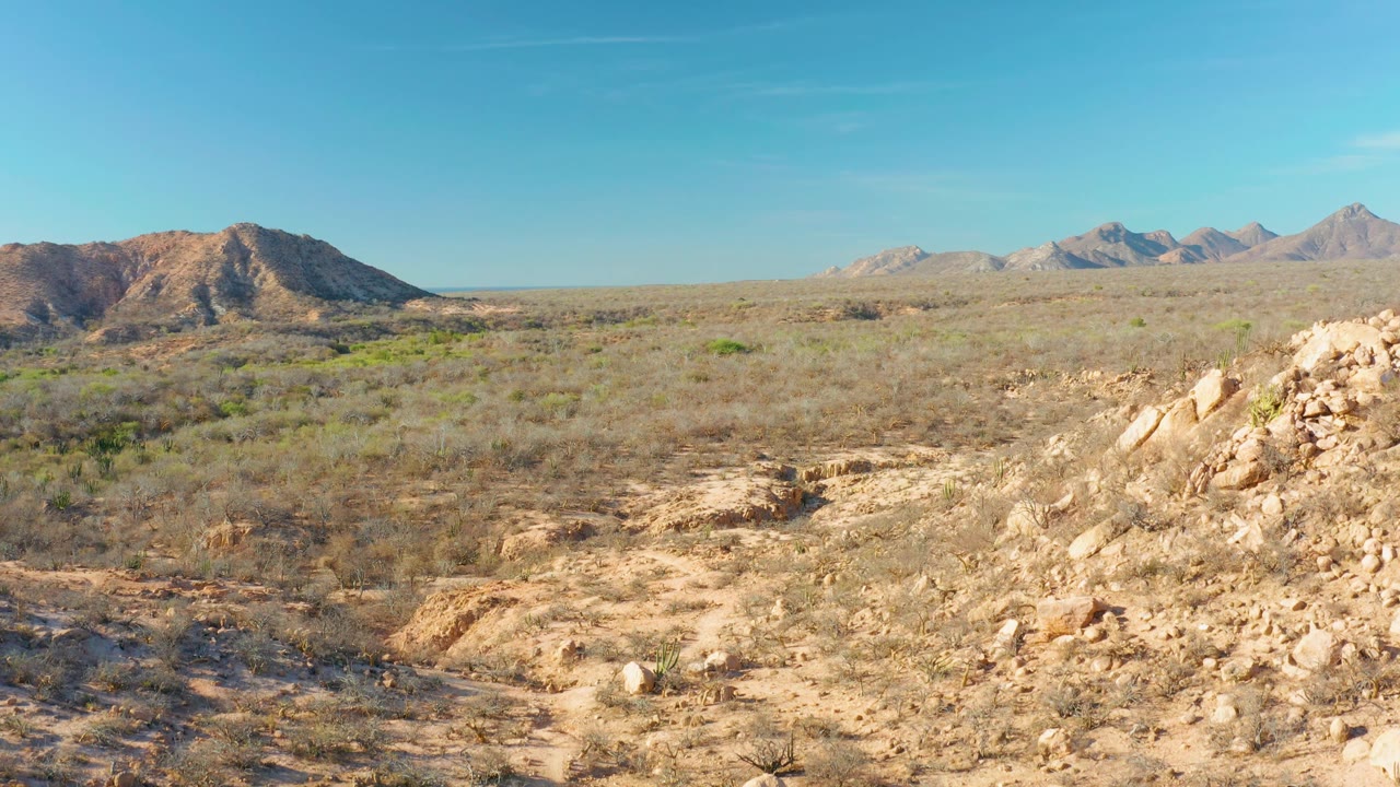 Broad dry valley with rocky outcrop, low shrubs, and distant mountains.