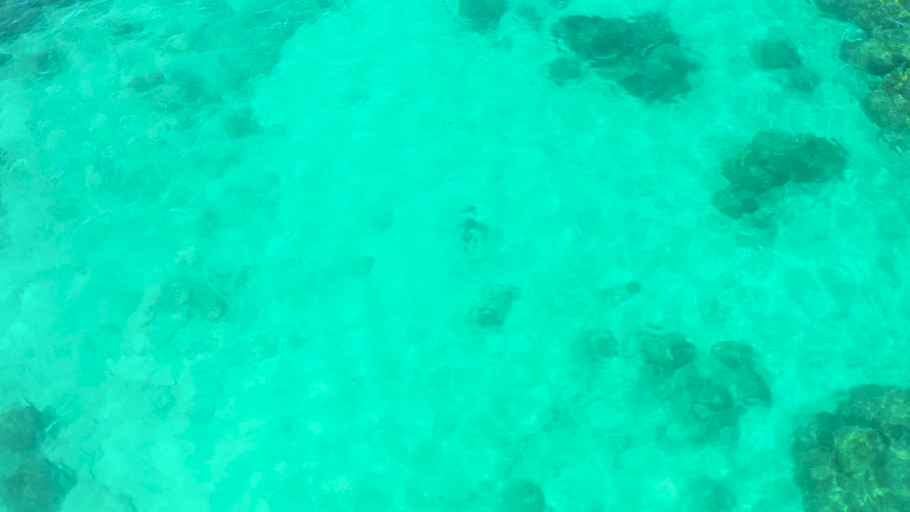 Turquoise sea surface in Cabo Pulmo, Mexico, shows the pale seabed below with larger dark underwater patches toward the upper frame and no visible people.