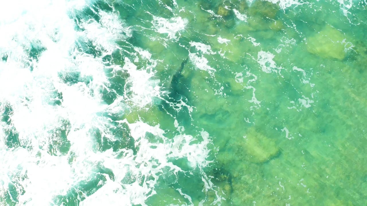 White surf foam over clear turquoise water and submerged rocks.