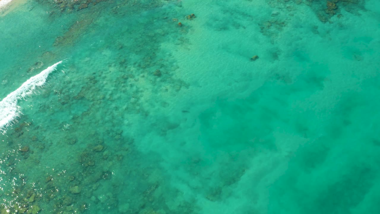 Turquoise ocean water over coral with small white foam at the left edge.