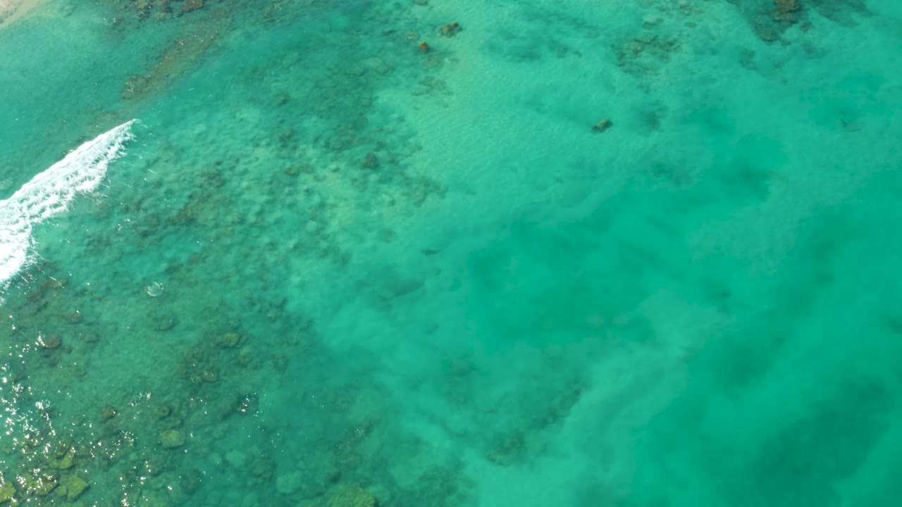 Overhead Cabo Pulmo ocean view with a brighter band of white foam near the upper left and darker coral formations visible through green-blue water, no visible people.