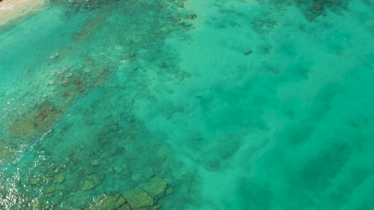 Overhead ocean surface with visible rocks beneath turquoise water.