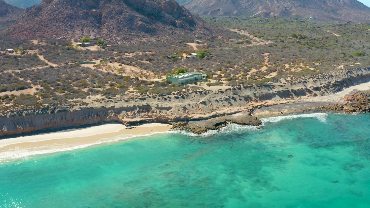Turquoise water and white surf below a rocky cliff and dry coastal hills.