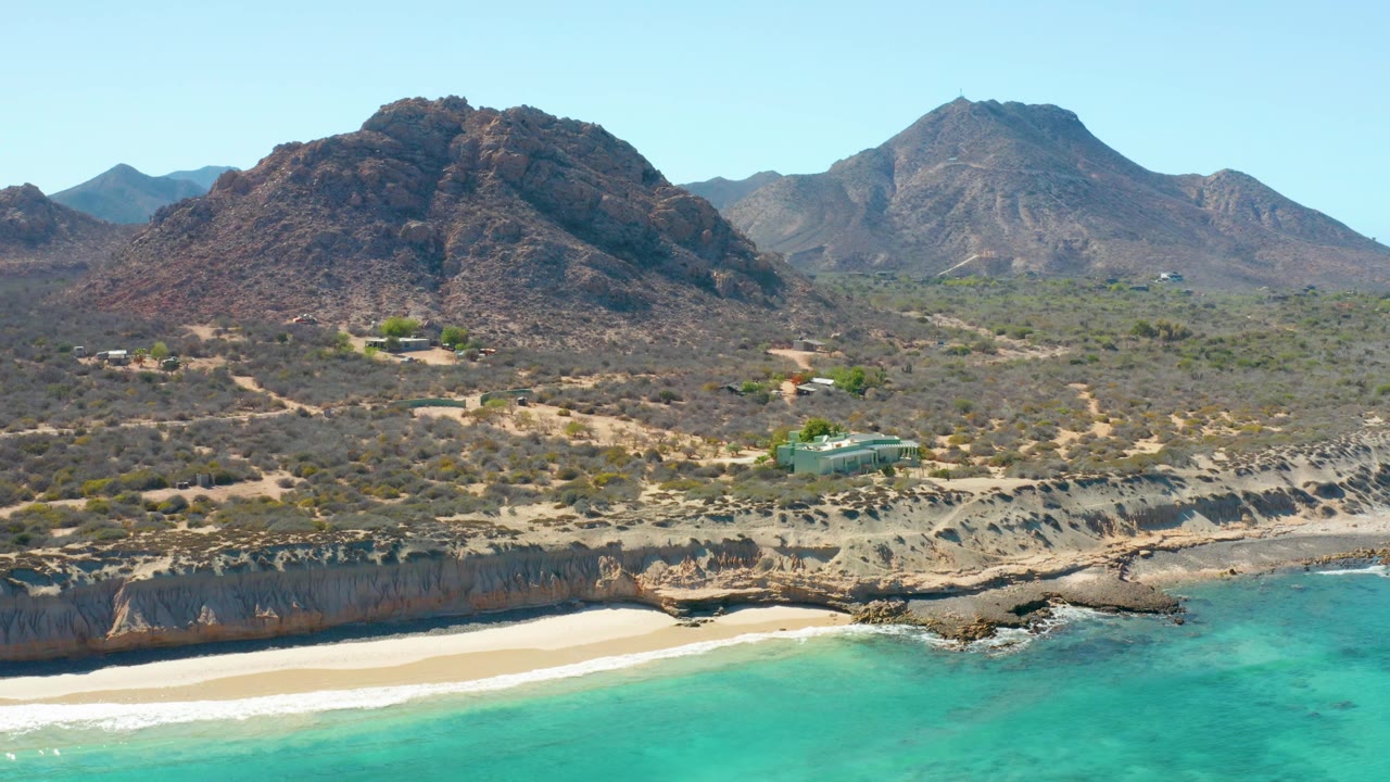 Closer aerial composition of mountains, scrubland, cliffs, beach, and turquoise ocean.