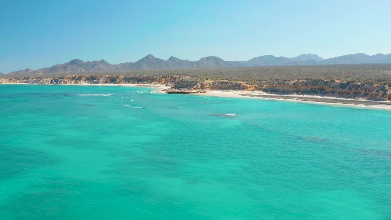 Turquoise ocean, sandy beach, rocky shore, and distant mountains