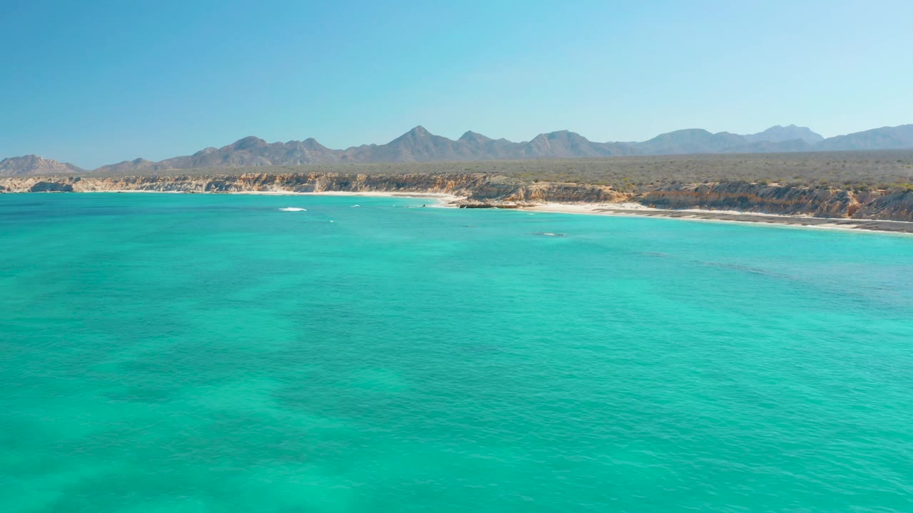 Cabo Pulmo turquoise water stretches toward a pale beach and distant desert mountains under a clear sky, with no visible people.