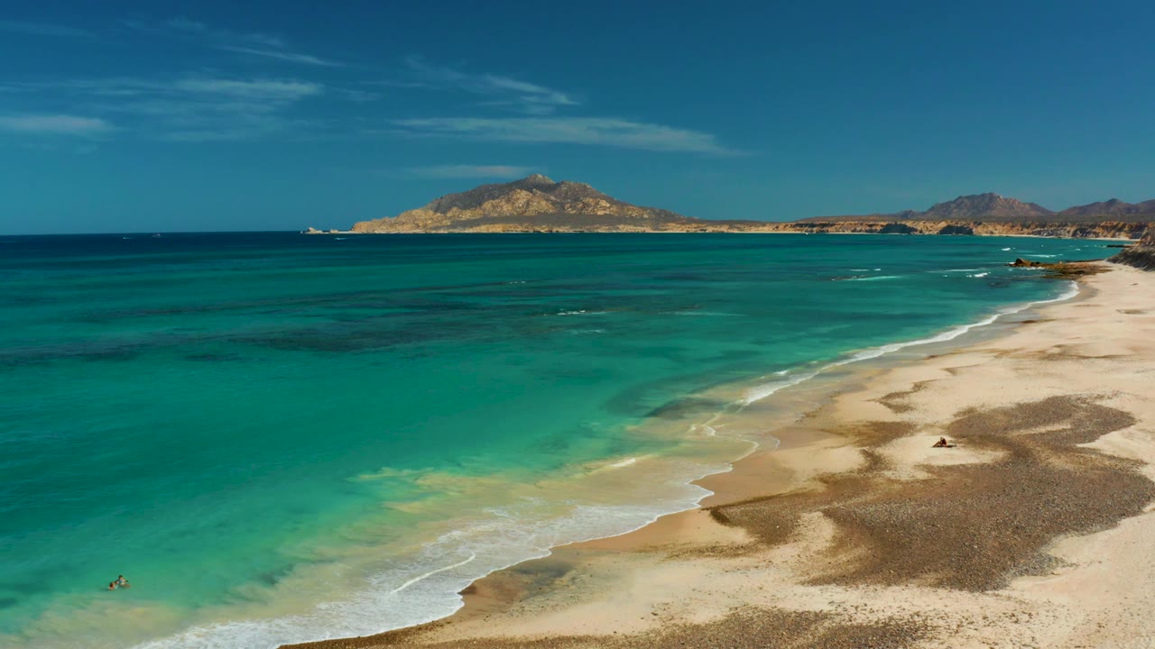 Clear water and pale beach with a small swimmer near shore