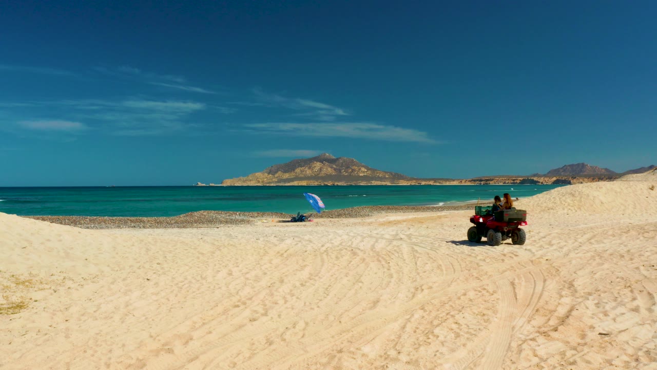 ATV on open sand with a blue umbrella near the waterline.
