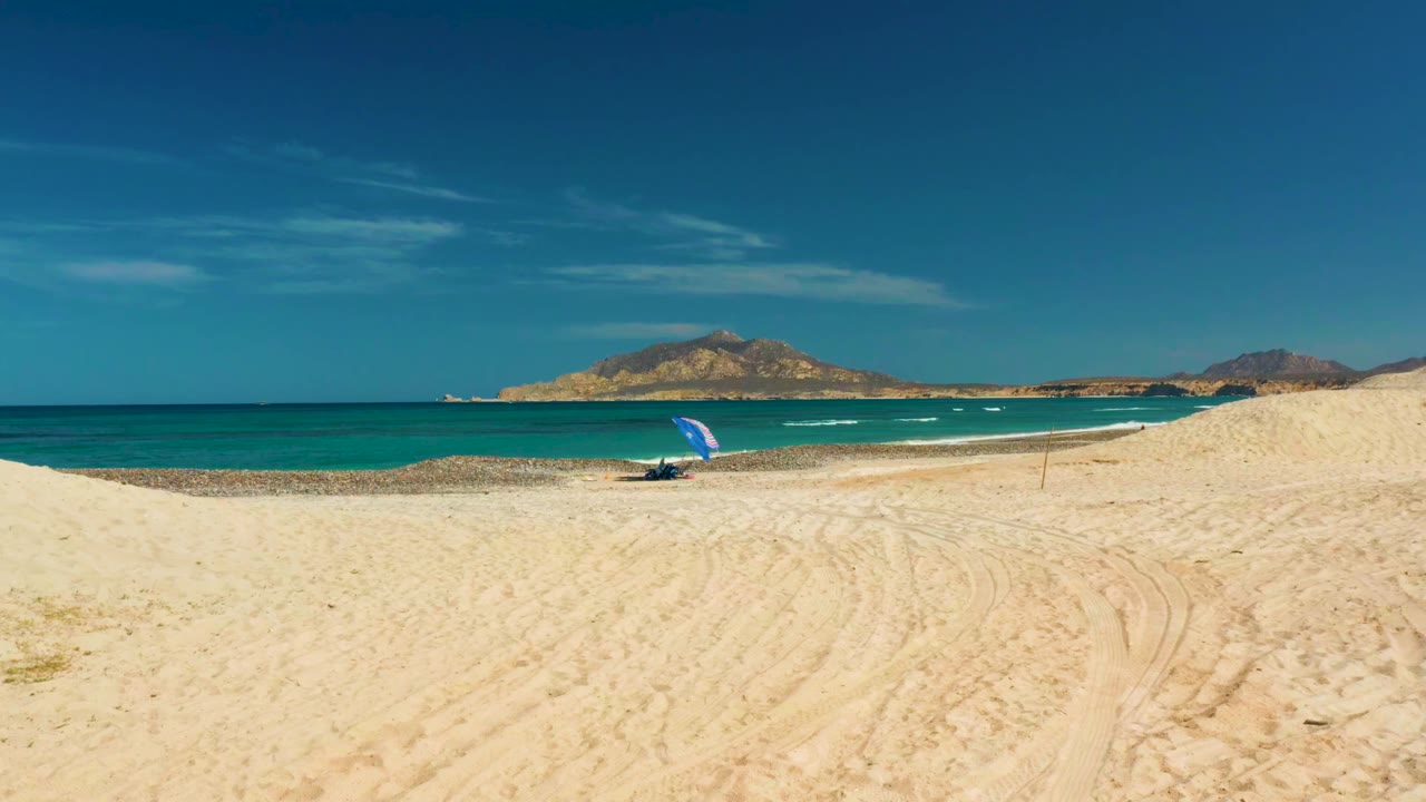 Beach and ocean view with blue umbrella and tire tracks in sand