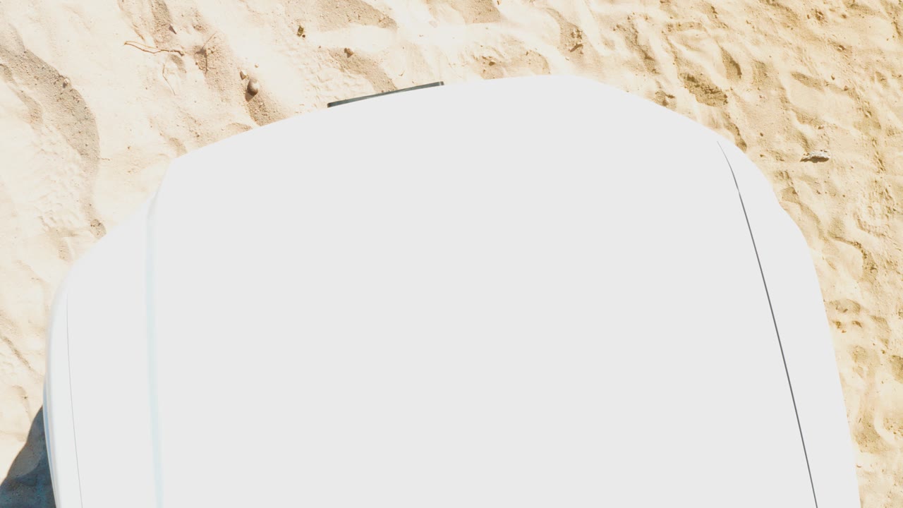 Overhead view one second in, with the rounded white chair surface dominating the frame and textured Cabo Pulmo sand visible above it, with no visible people.