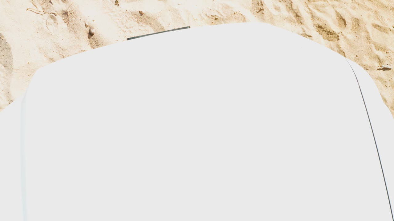 Mid-clip overhead frame where the white lounge chair nearly fills the lower image and sunlit Cabo Pulmo sand forms a narrow band above, with no visible people.