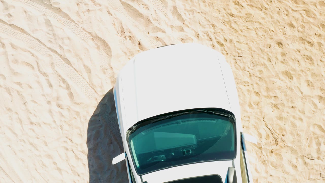 White car advancing under an overhead camera on sand.