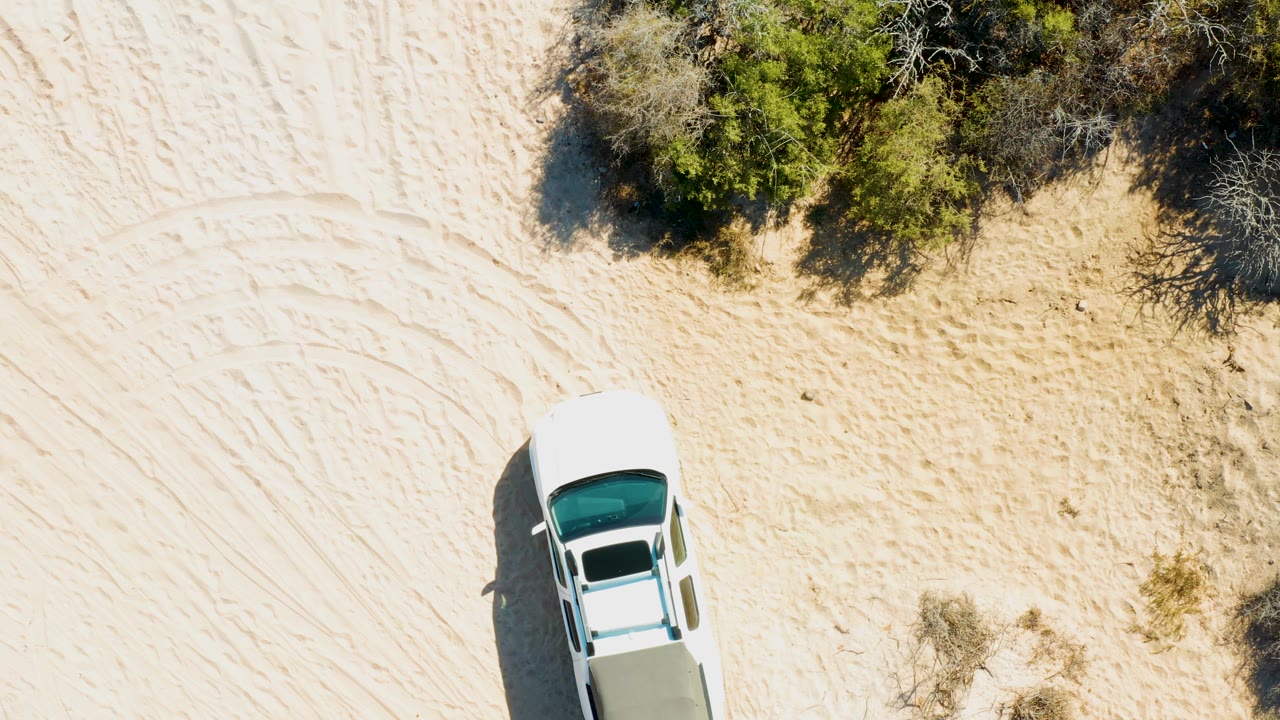 White pickup partly near the lower edge with dense bushes and sandy tracks above.