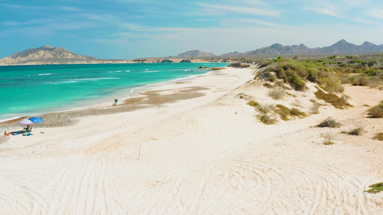 Beachgoers on open sand near turquoise water and low surf.