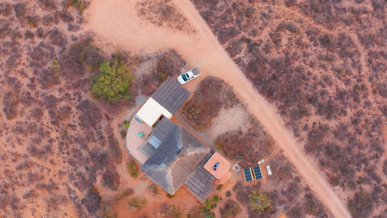 Overhead desert house scene with a pale road, white car, and sparse vegetation.