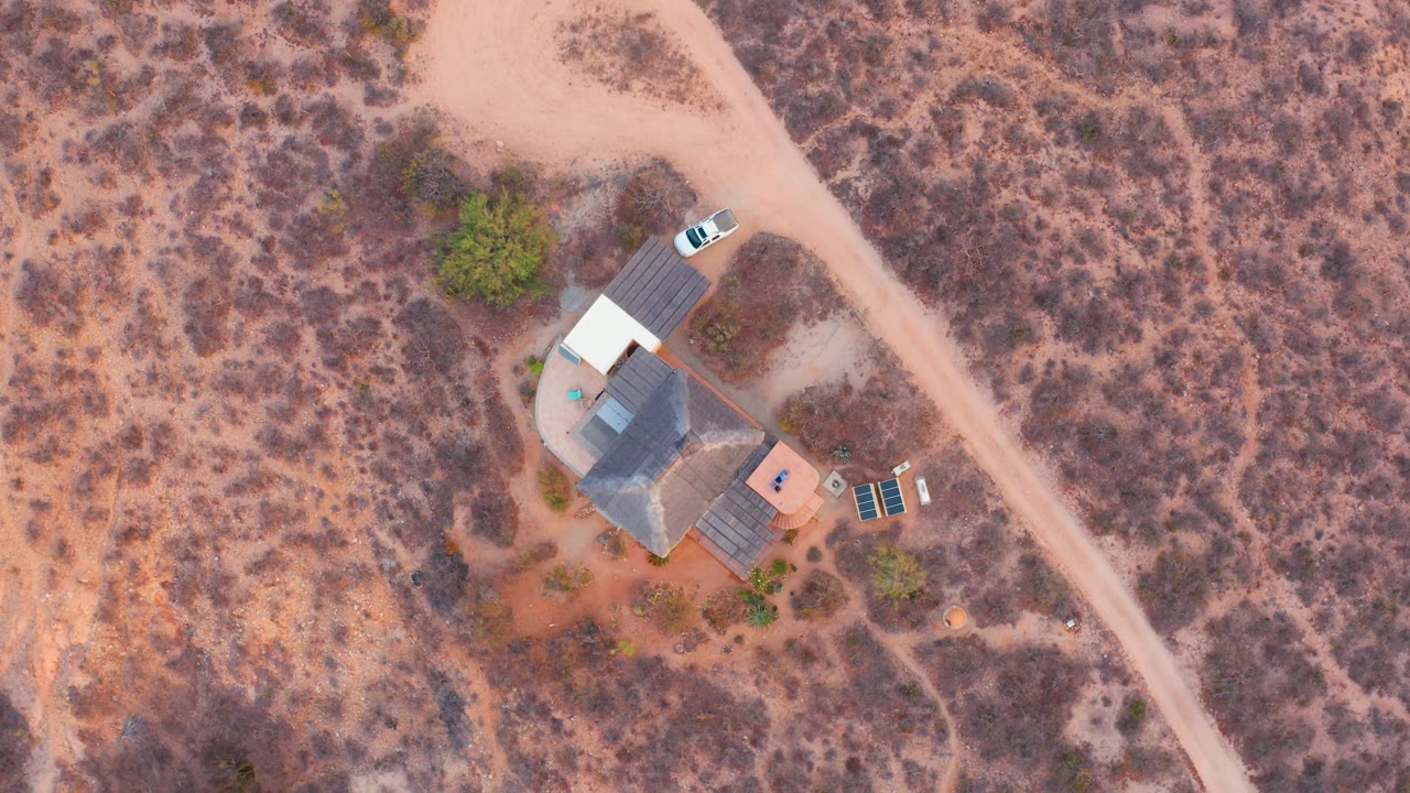 Aerial view of a white car by a desert house and diagonal dirt road.