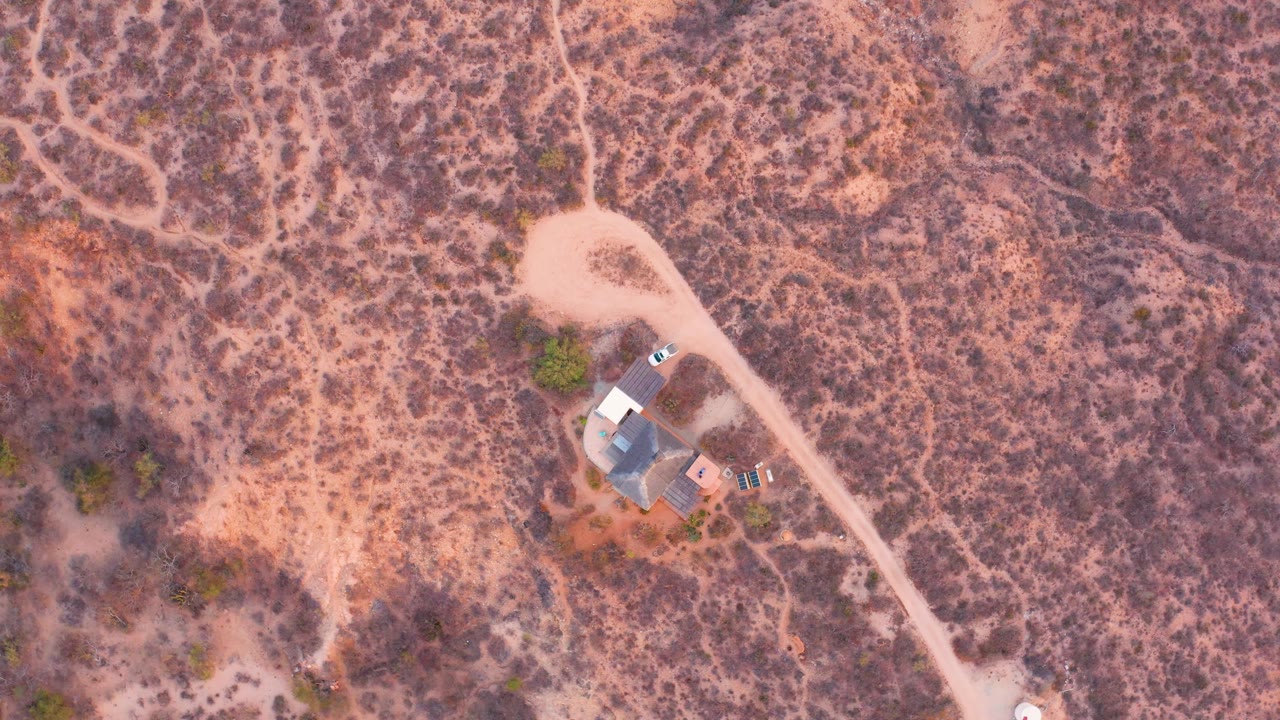Aerial view of a house beside a pale dirt road in scrubland.