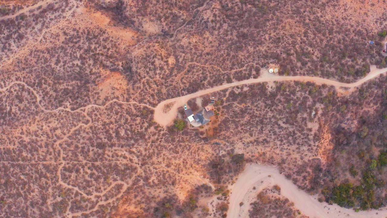 Overhead view in Cabo Pulmo, Baja California Sur, Mexico, showing a small house near pale dirt roads across dry scrubland with no visible people.