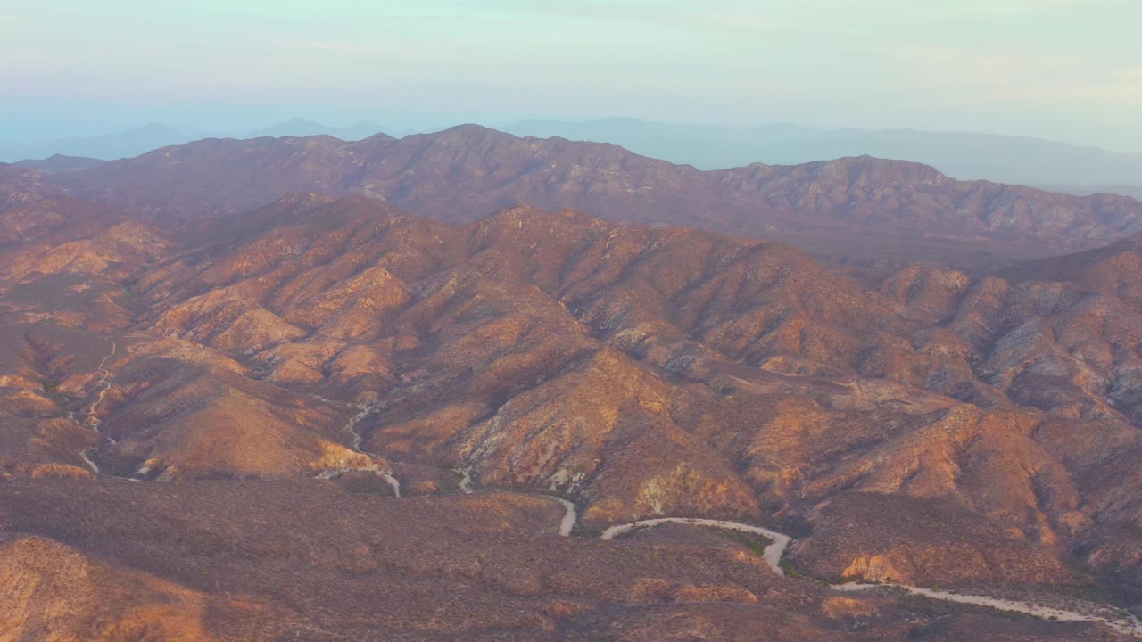 Dry mountain valley with winding road and distant peaks