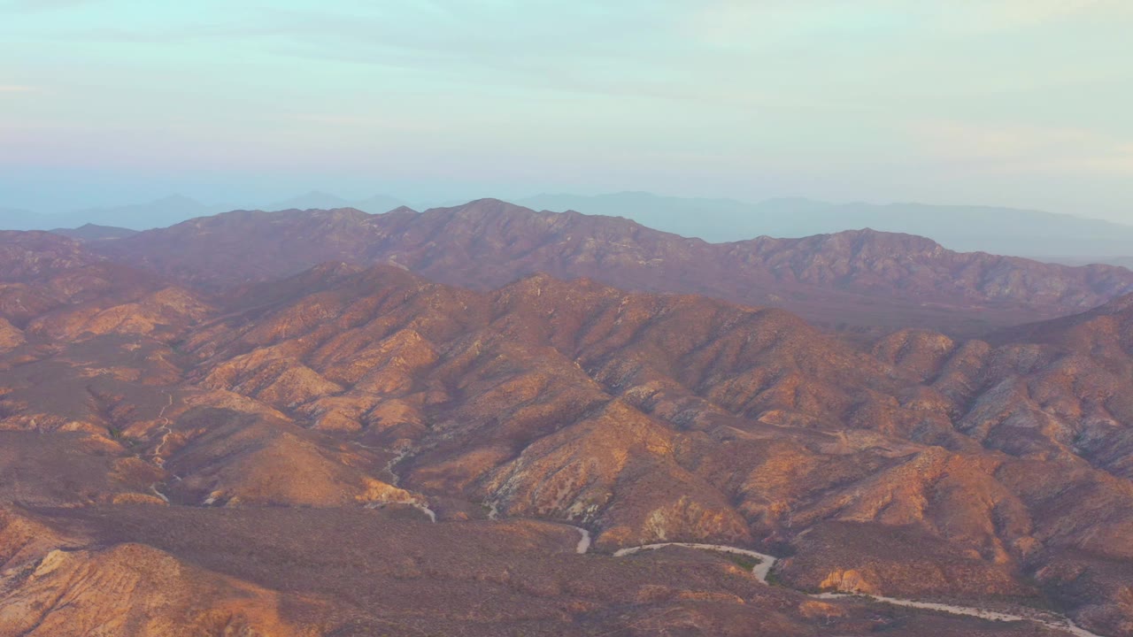 Aerial view of rugged brown mountains beneath pale sky.