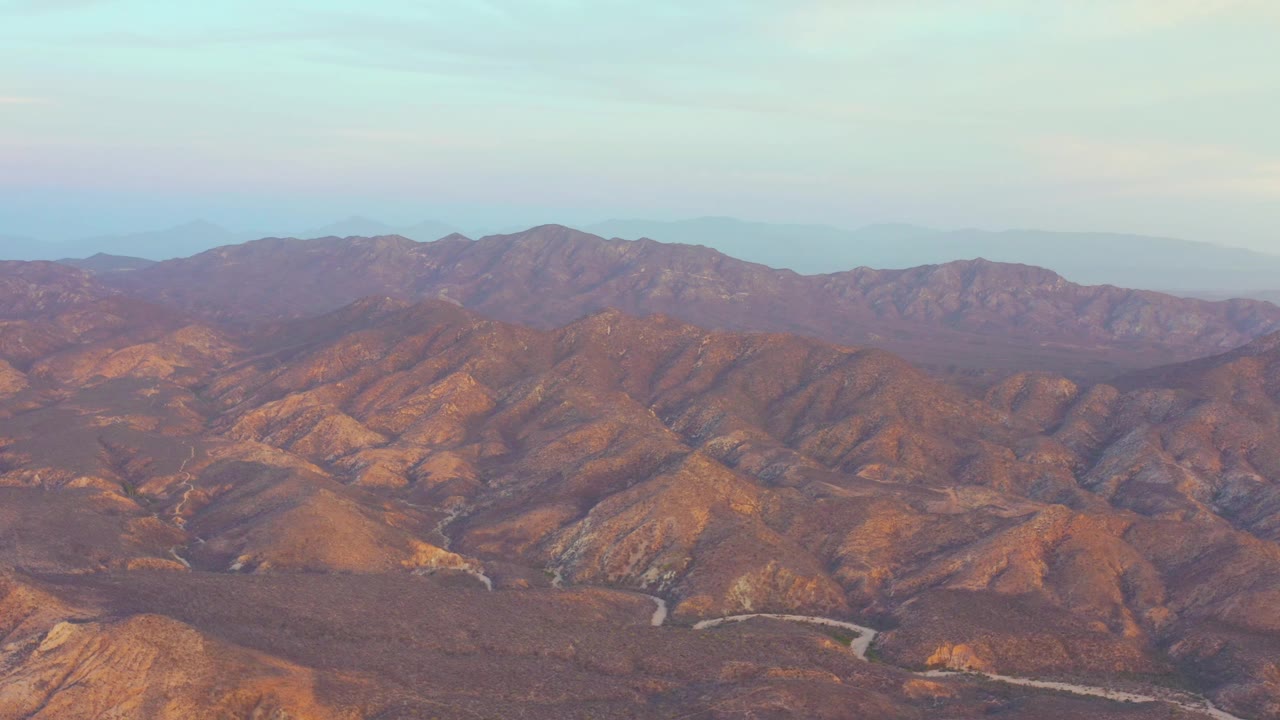 Cabo Pulmo aerial frame showing layered brown ridges, a pale riverbed curving through the valley, and no visible people.