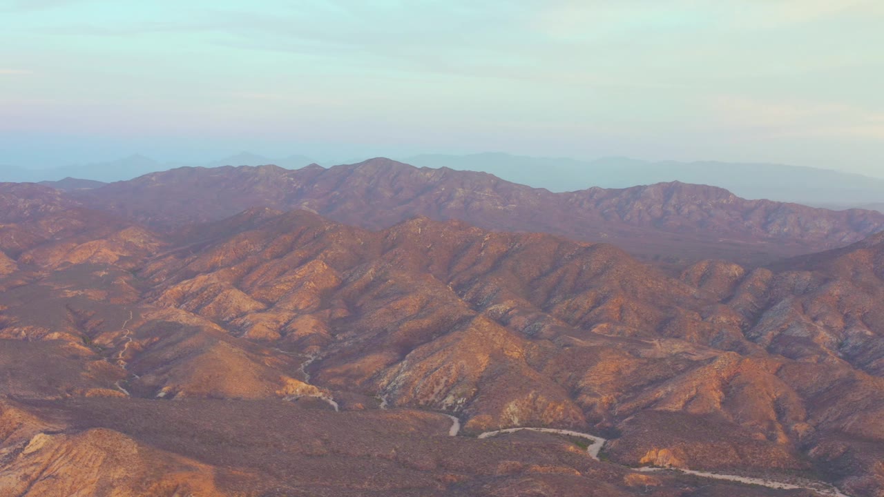 Wide Cabo Pulmo mountain view with orange-lit slopes in the foreground, darker ridges beyond, pale sky, and no visible people.