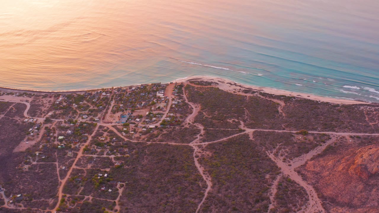 Aerial beach and inland desert settlement with warm light on the water.