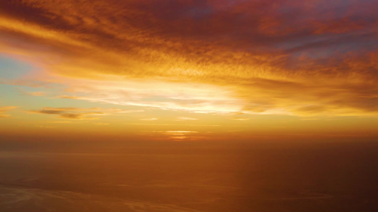 A warm sunset glow spreads across the flat ocean horizon at Cabo Pulmo, with layered orange and pink clouds overhead and no visible people.