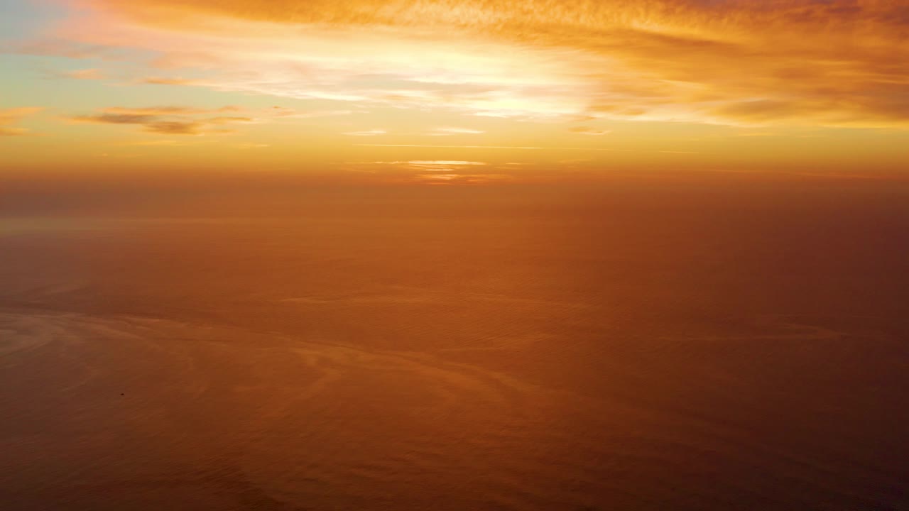 Golden sunset over a calm ocean horizon with orange clouds.