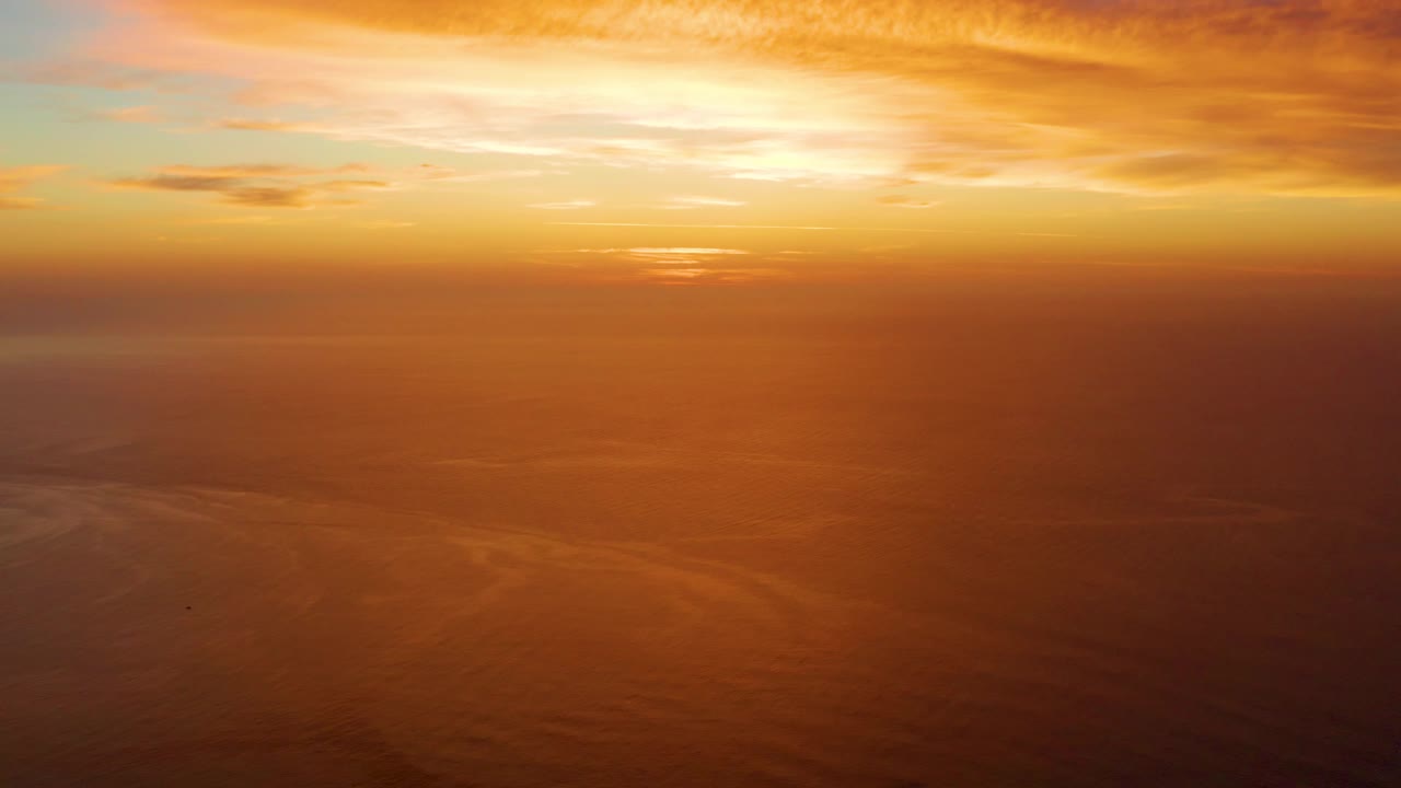 A bright band of sunset light sits near the horizon over still ocean water in Cabo Pulmo, with orange clouds above and no visible people.