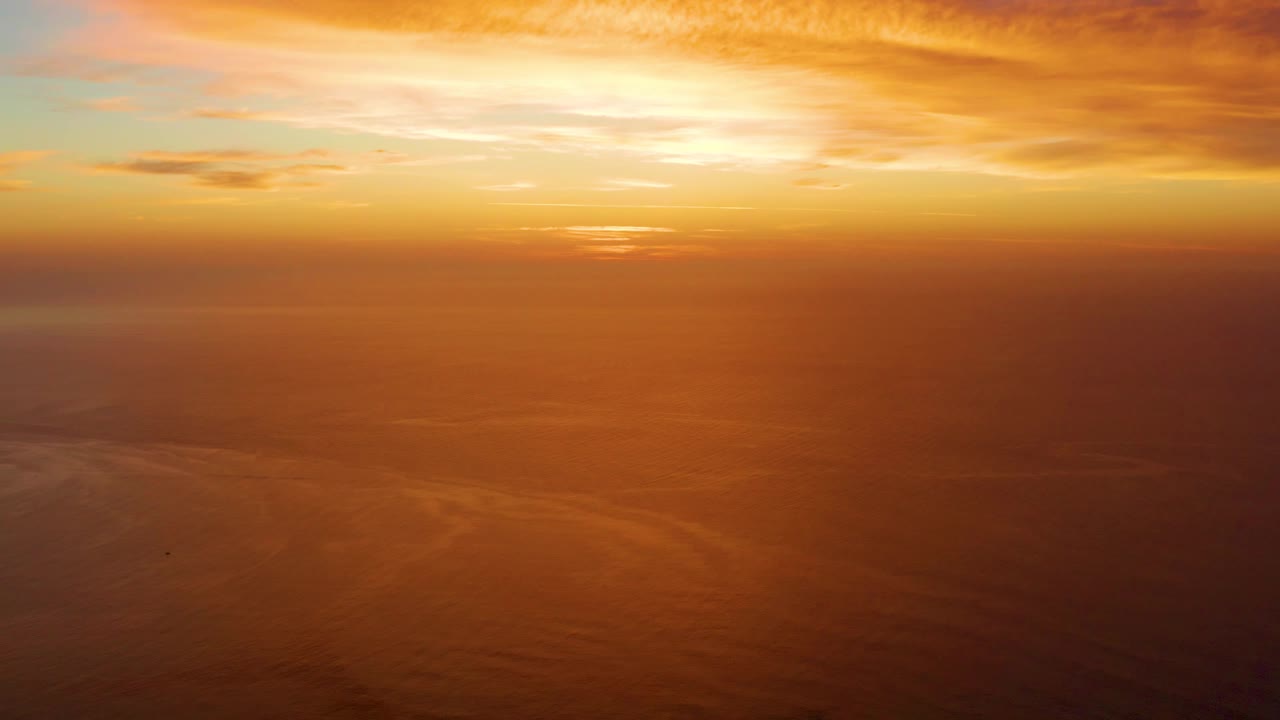 Warm gold and orange clouds stretch over a reflective ocean surface in Cabo Pulmo, with no landforms, vessels, or people visible.