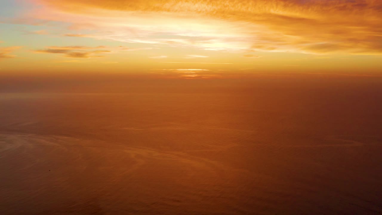 Golden orange clouds sit above a hazy ocean horizon in Cabo Pulmo, Baja California Sur, with calm water below and no visible people.