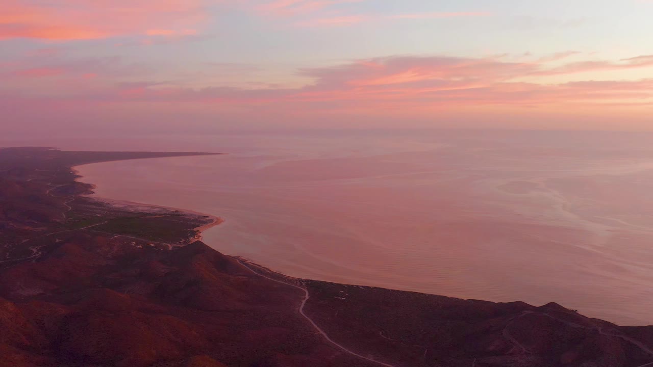 Sunset over coastal hills, winding road, and calm sea.