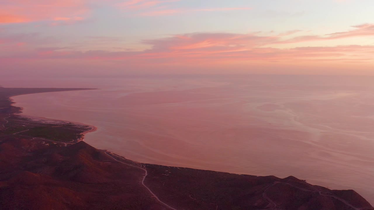 Coastal hills and calm water under orange-pink dusk clouds.