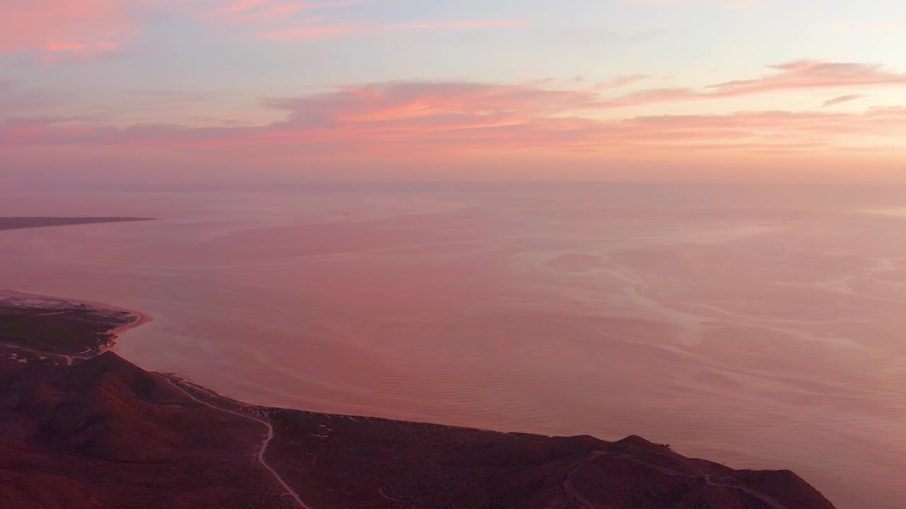 Aerial Cabo Pulmo sunset frame with the ocean dominating the view, a dark coastal slope below, a pale shoreline track, and no visible people.