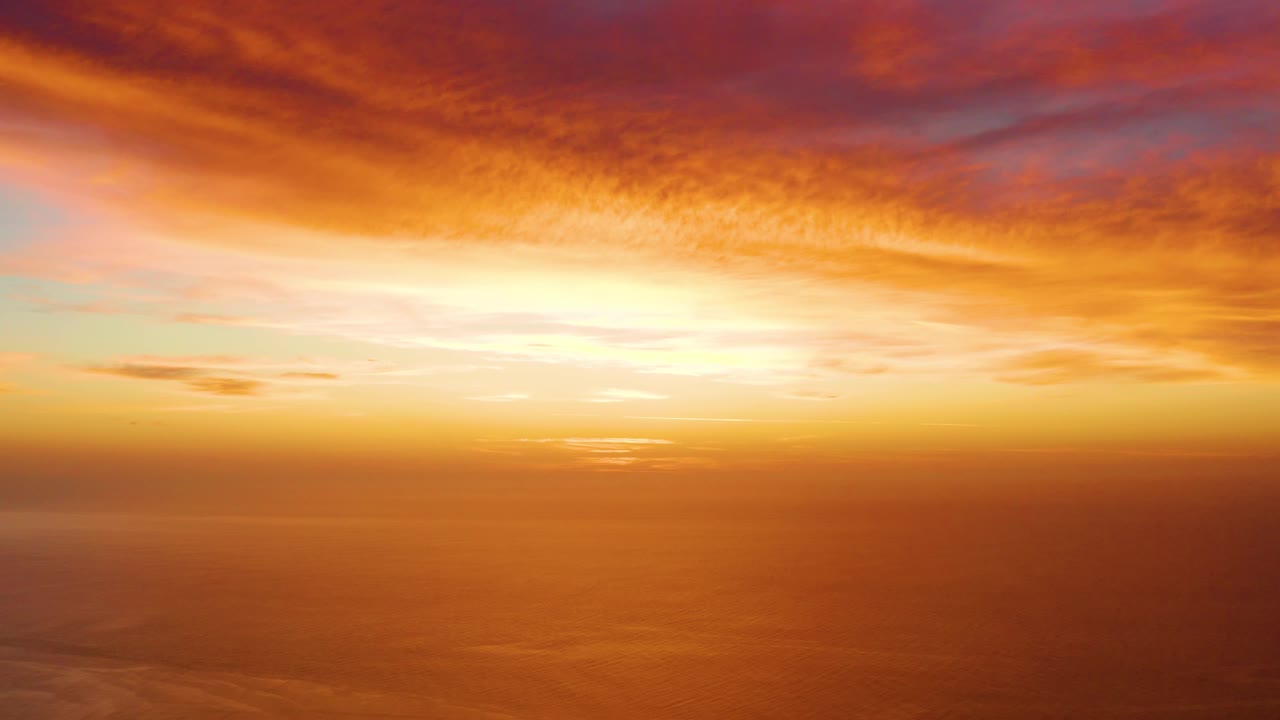 Opening frame of a Cabo Pulmo sunset with orange and pink clouds above a calm hazy ocean horizon and no visible people.