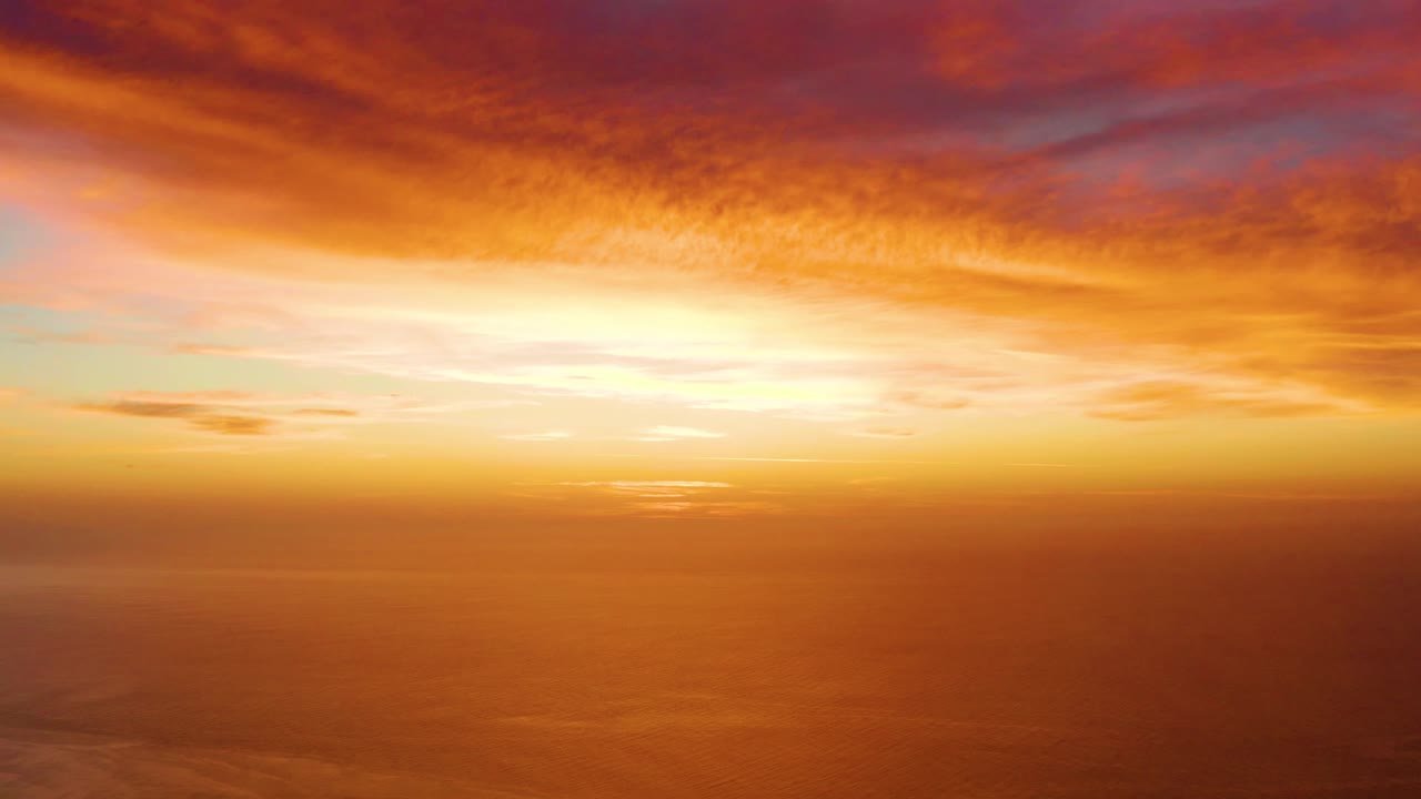 Opening frame of a Cabo Pulmo sunset with orange cloud cover, a bright low horizon glow, calm ocean below, and no visible people.