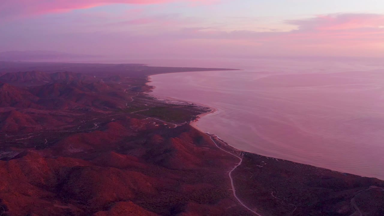 Red mountain coastline and calm water under purple pink sky.