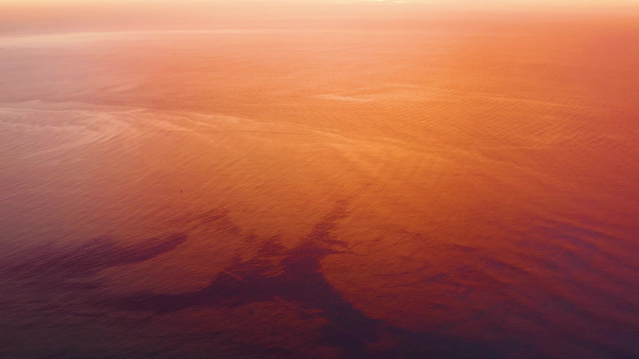 Cabo Pulmo water surface one second in, with a pale reflection band near the top, orange ripples through the center, darker lower water, and no visible people.