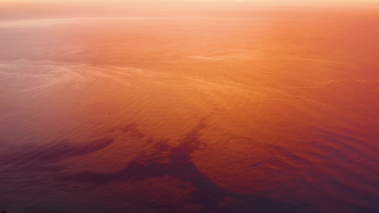 Cabo Pulmo water at 0:03, showing a broad orange reflective field, darker sheen-like forms in the lower third, and no visible people.