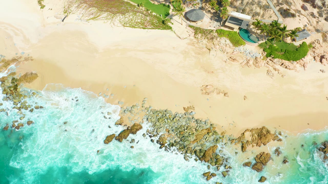 Overhead sandy beach with surf foam crossing rocky shoreline