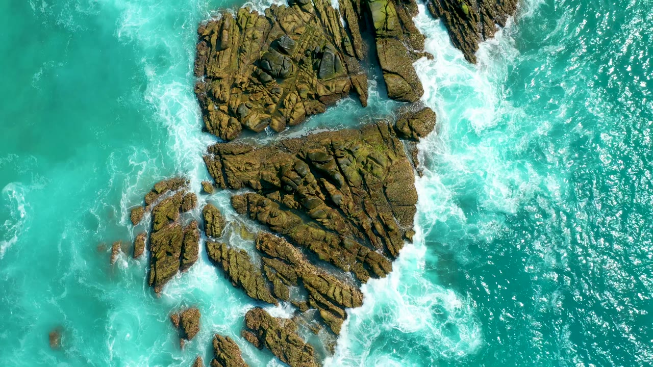 Aerial frame at Marquis Los Cabos with white foam pushing through channels between brown rock outcrops and green-blue water, with no visible people.