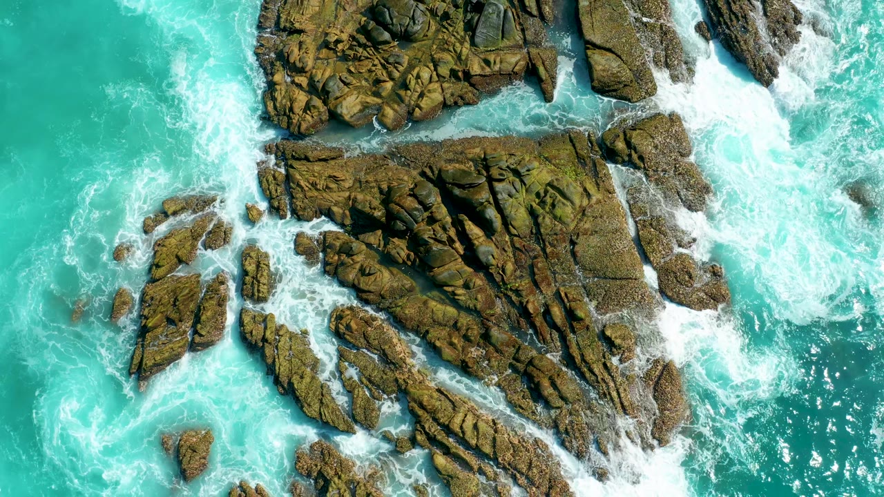 Aerial surf and rocks with foam wrapping around stone edges