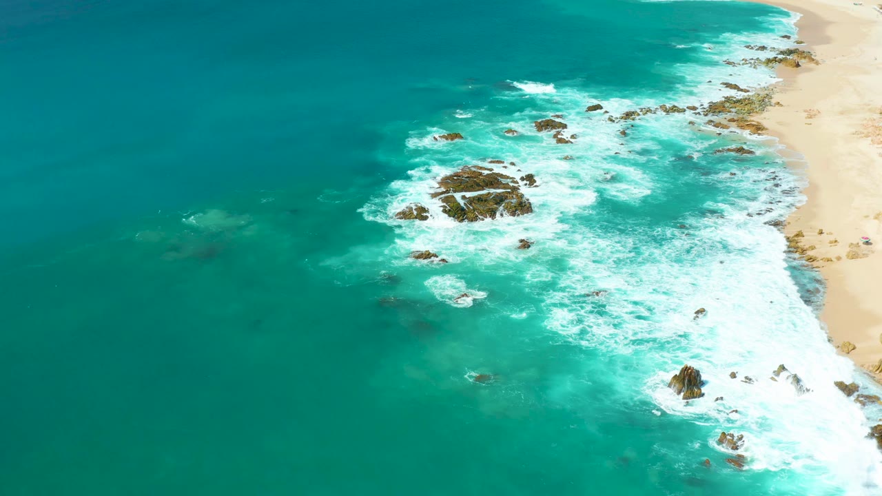 Turquoise water and white foam spread around rocky outcrops near shore.