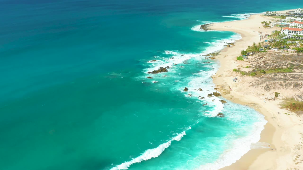 Aerial coastline view with open turquoise water, rocks, and sandy beach.