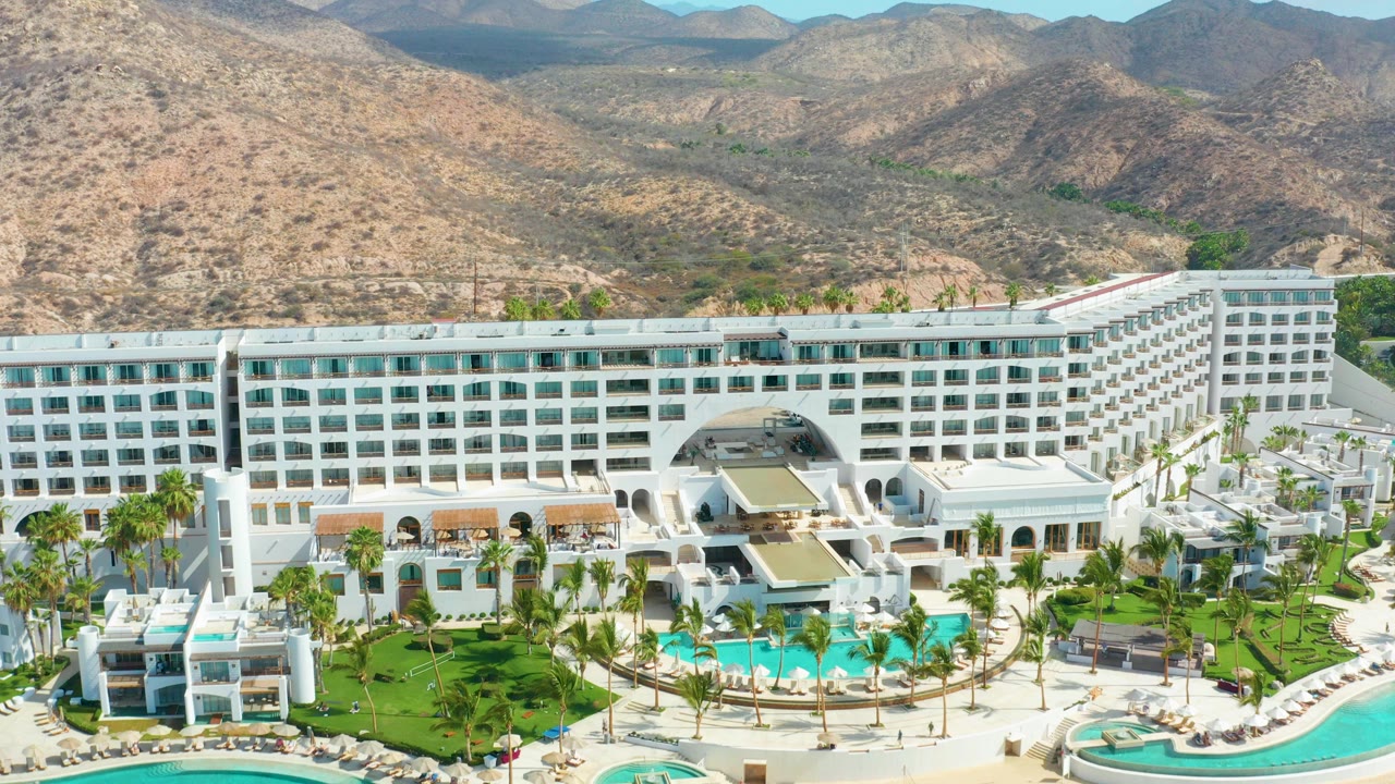 Aerial view of white hotel complex with pools and desert mountains